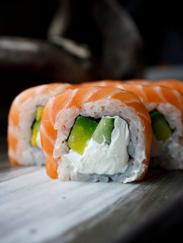 Delicious salmon sushi roll with avocado and cream cheese on wooden board.