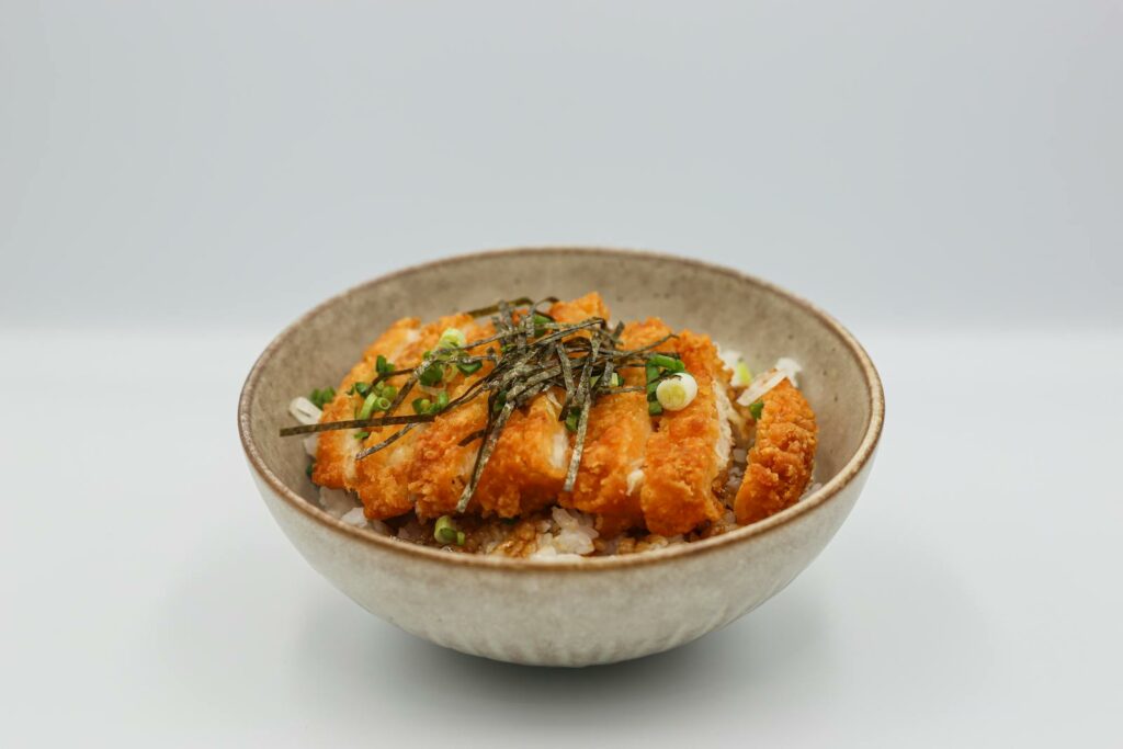 A mouthwatering chicken katsu served on steamed rice with savory toppings in a bowl.