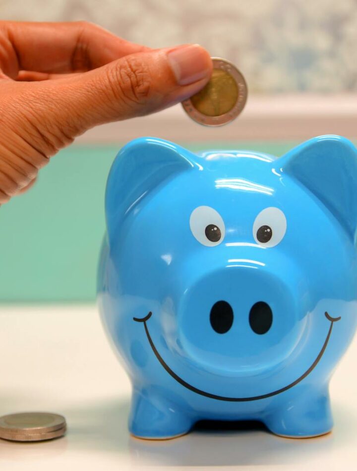 Hand inserting a coin into a blue piggy bank for savings and money management.