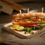 Mouth-watering sandwich with vegetables and sausage on wooden board, perfect for a delicious meal.