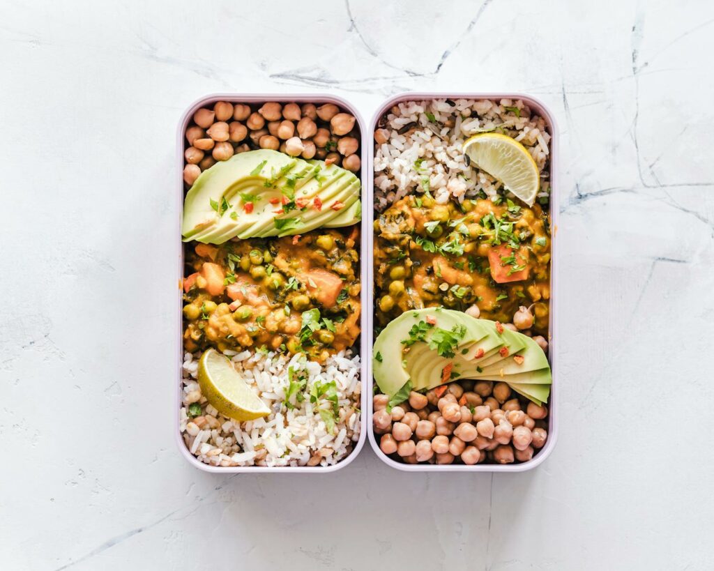 Delicious lunchboxes, bento boxes featuring chickpeas, rice, avocado, and curry on a white background.