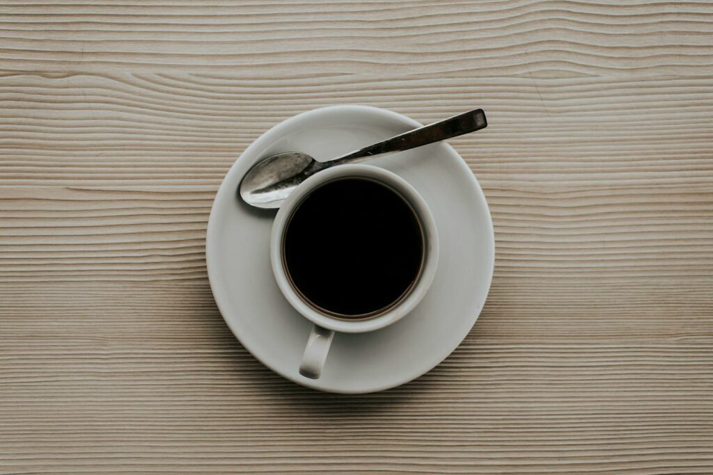 A coffee cup with a saucer and spoon on a textured wooden surface, viewed from above.