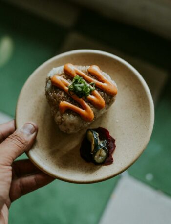 Close-up of gourmet onigiri with sauce on a small plate, held by human hand.