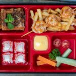 Delicious bento box featuring shrimps, sushi, fries, and fresh vegetables. Perfect for a unique meal.