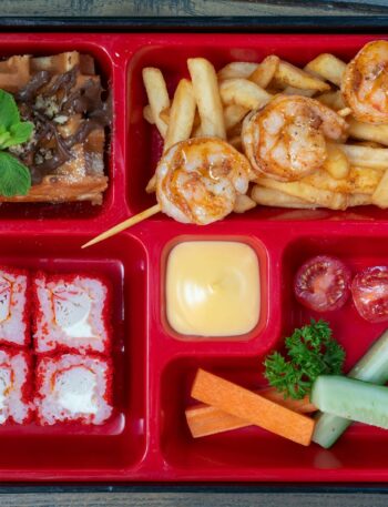 Delicious bento box featuring shrimps, sushi, fries, and fresh vegetables. Perfect for a unique meal.