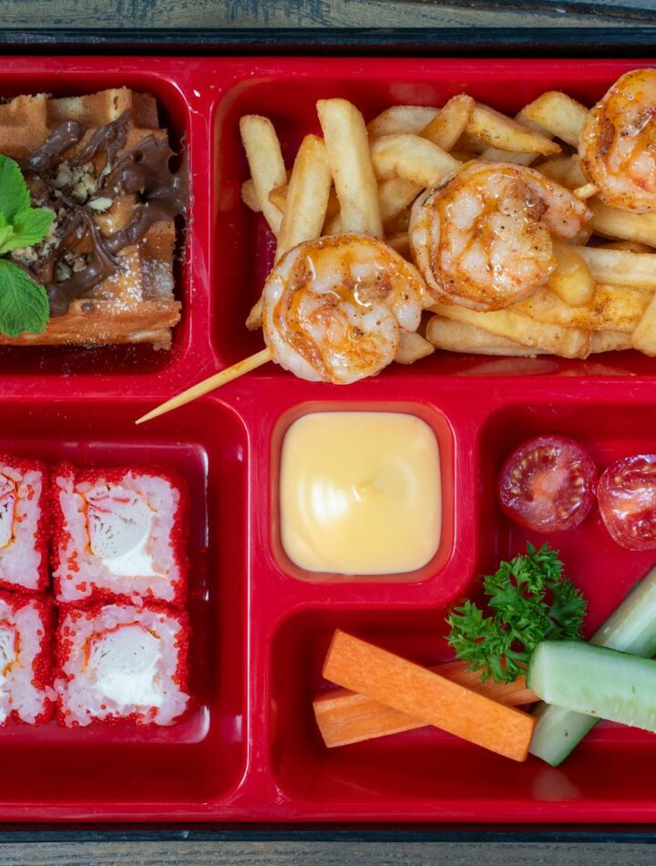 Delicious bento box featuring shrimps, sushi, fries, and fresh vegetables. Perfect for a unique meal.