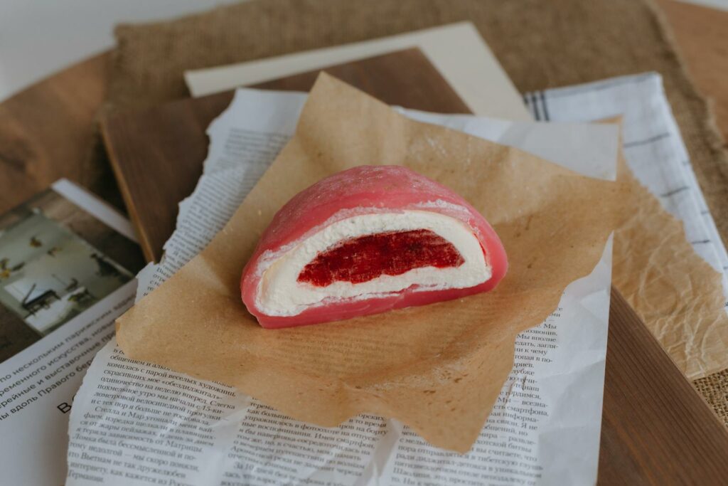 Close-up of a pink strawberry mochi dessert on rustic paper, showcasing its texture. japanese desserts