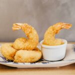 Golden crispy tempura shrimp beautifully plated on ceramic dish. tempura dipping sauce