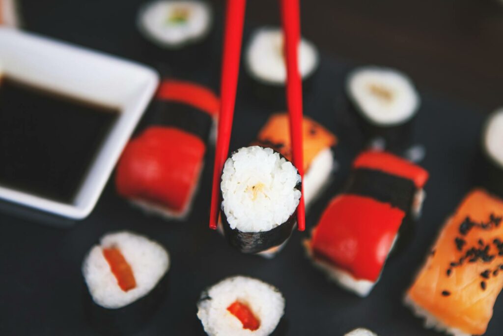 A selection of various sushi rolls with chopsticks on a dark plate, featuring vivid colors and fresh ingredients.