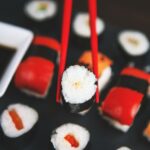 A selection of various sushi rolls with chopsticks on a dark plate, featuring vivid colors and fresh ingredients.