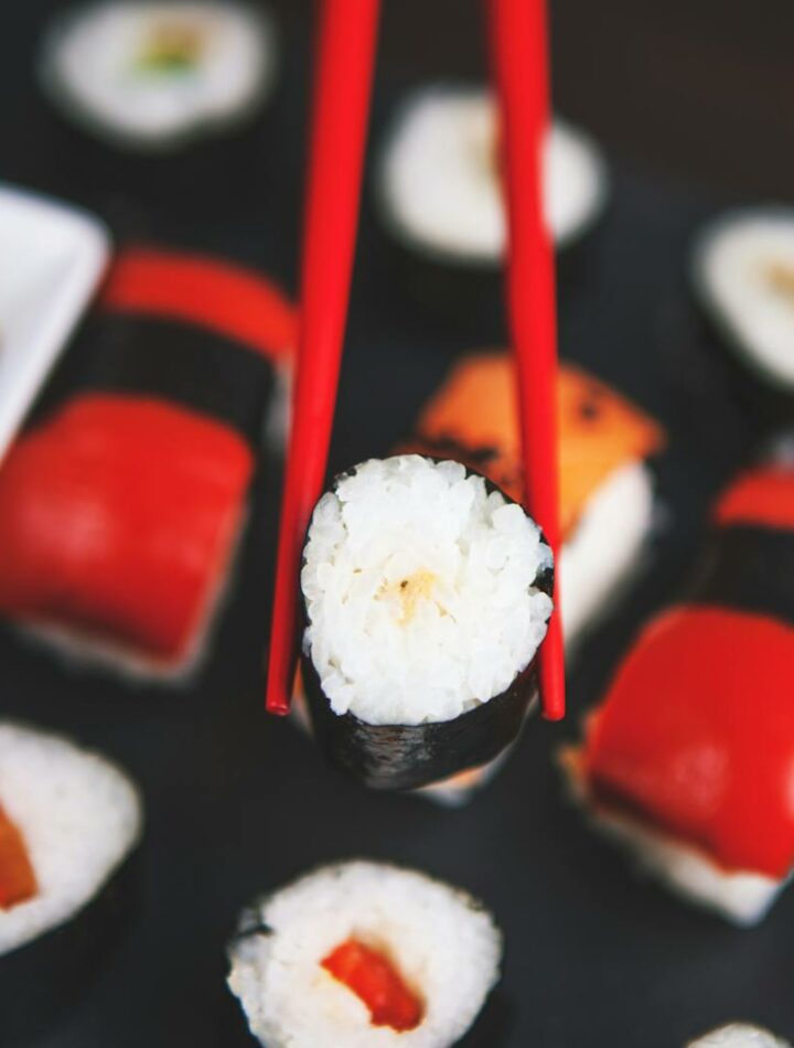 A selection of various sushi rolls with chopsticks on a dark plate, featuring vivid colors and fresh ingredients.