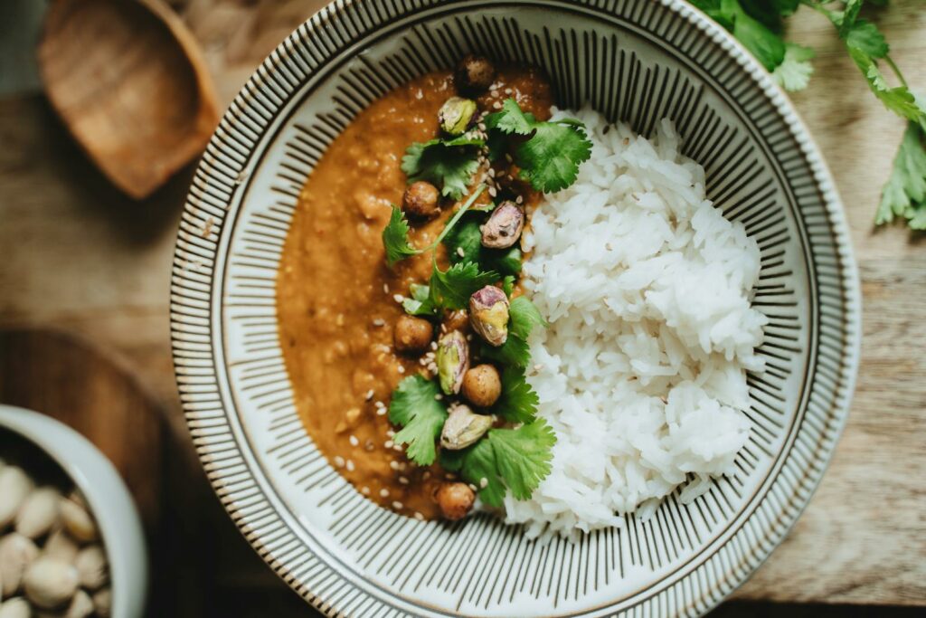 Delicious vegan rice bowl featuring lentil curry, topped with pistachios, cilantro, and sesame seeds, japanese rice.