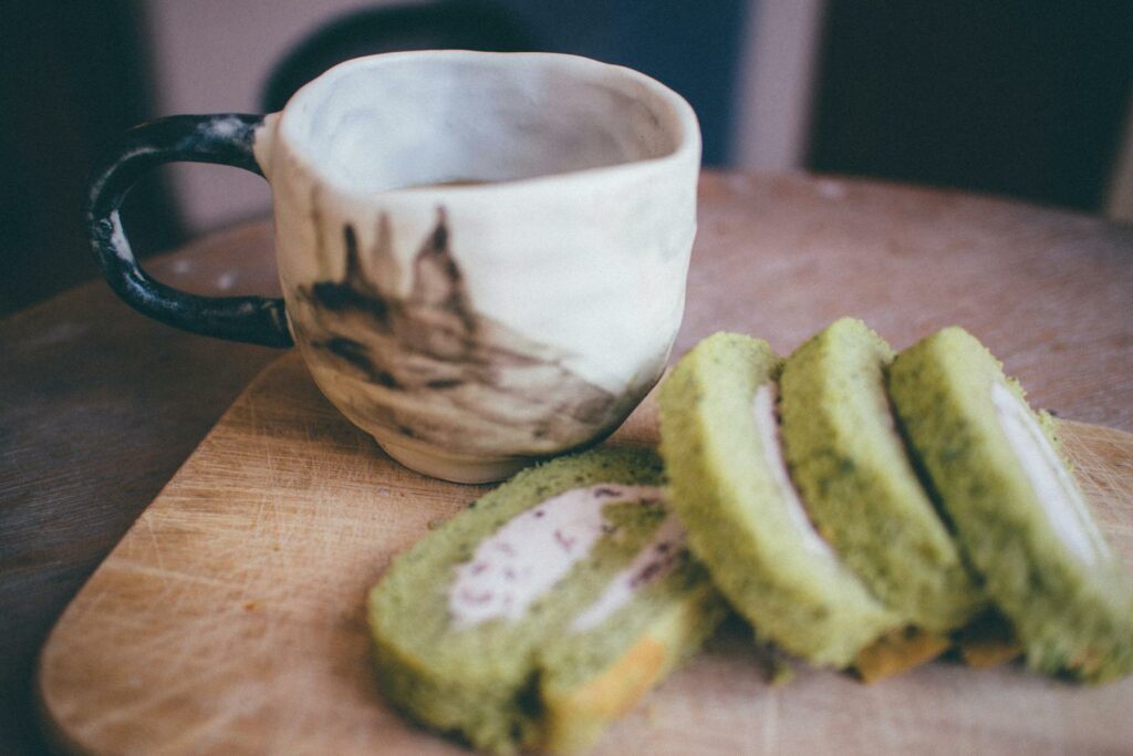 Sliced matcha roll cake on wooden board with ceramic tea cup. Warm, inviting composition.