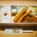 A Japanese bento box featuring rice, prawns, and salad, perfect for lunch or dinner.