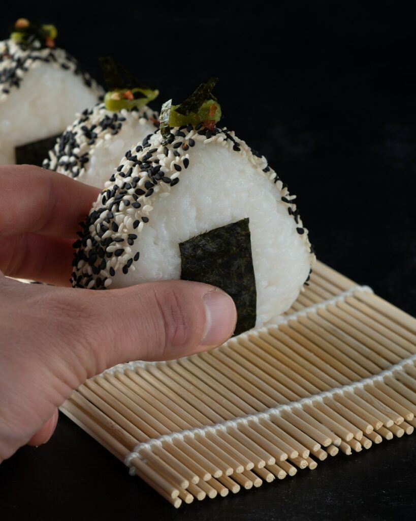 person holding white and brown cake onigiri, japanese bento box